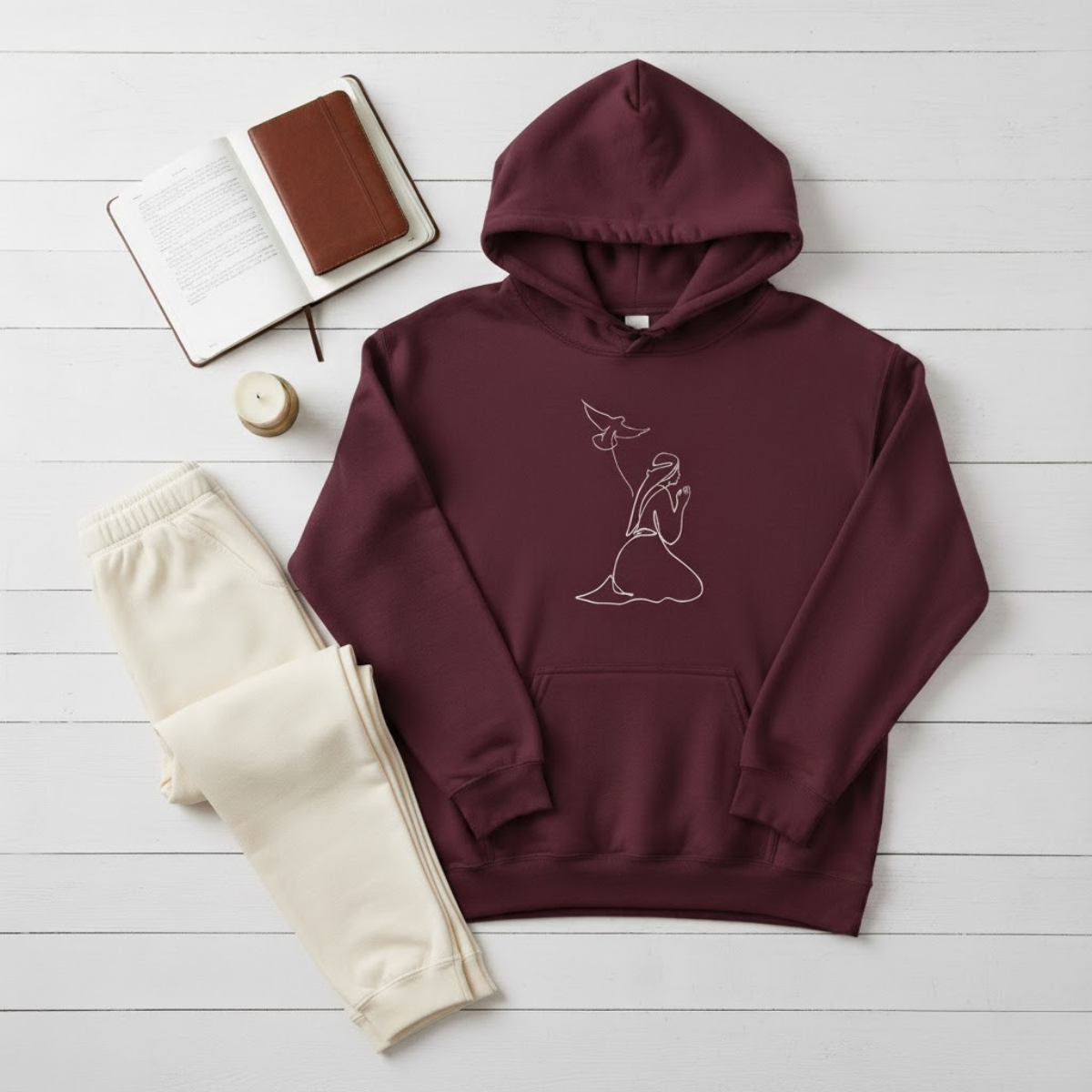 Burgundy women’s hoodie featuring minimalist line-art of Mary praying with the Holy Spirit as a dove — faith-inspired Catholic apparel for women.